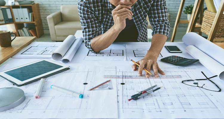 architect inspecting multiple building plans on a table