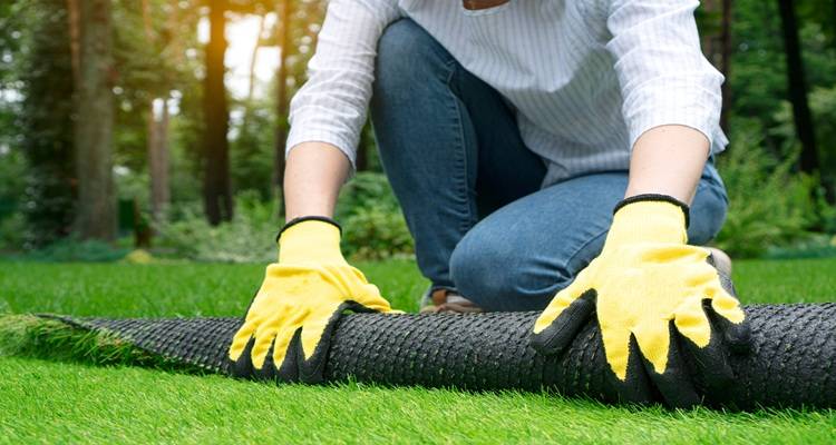 yellow gloved hands installing fake grass