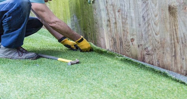 man laying fake grass next to fence
