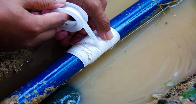 Hand applying PTFE tape to a blue pipe