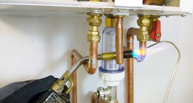 boiler installation cost guide &mdash; closeup of a new boiler being fitted by a tradesperson