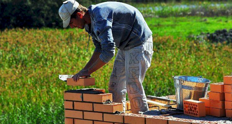 bricklayer working on building brick wall in garden