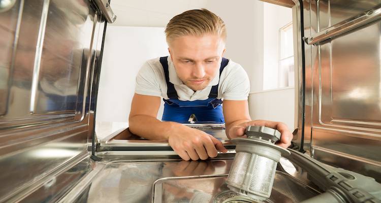 tradesperson installing a component inside of a new dishwasher unit