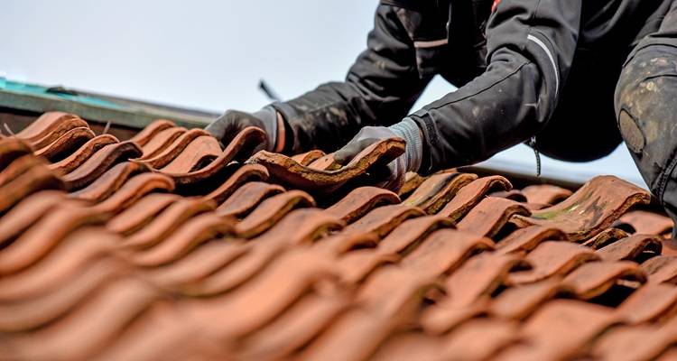Hands repairing red roof tiles