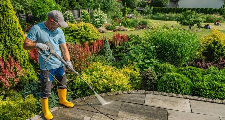 man jetwashing patio with garden background