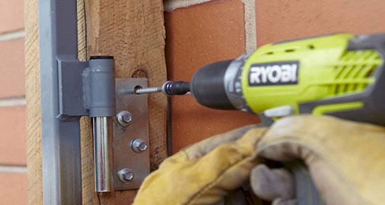 person using a drill to hang a gate to a wooden gate post