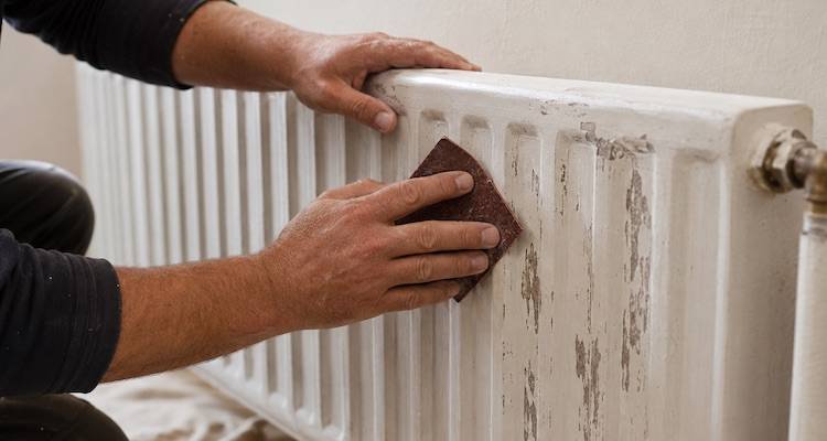 tradesperson sanding a radiator to prepare it for a new coat of paint
