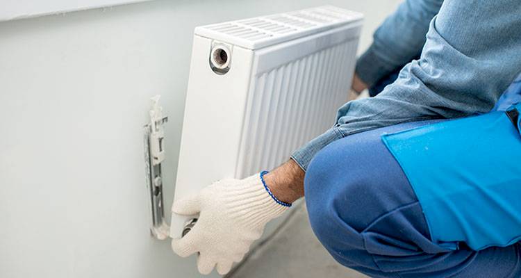 central heating installation cost guide &mdash; tradesperson fitting a new radiator to a radiator wall fixture