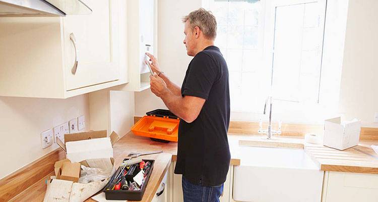 central heating installation cost guide &mdash; tradesperson installing a new boiler in a kitchen cabinet