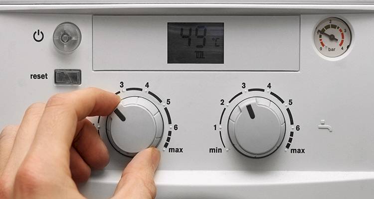 combi boiler installation cost guide &mdash; closeup of a hand adjusting the temperature on a boiler control panel