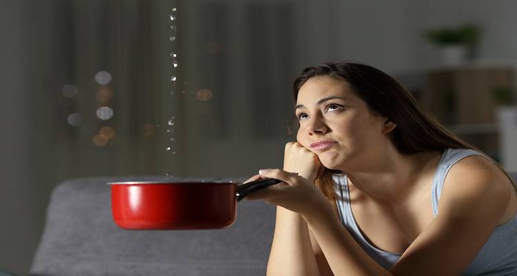 woman holding out a saucepan to catch water from a leak in home