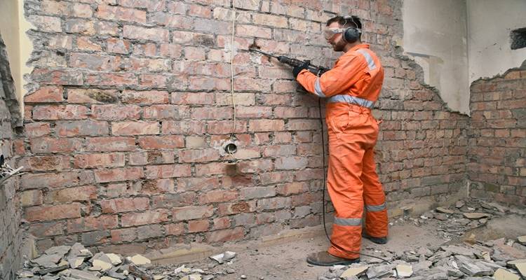 man in orange knocking off plaster