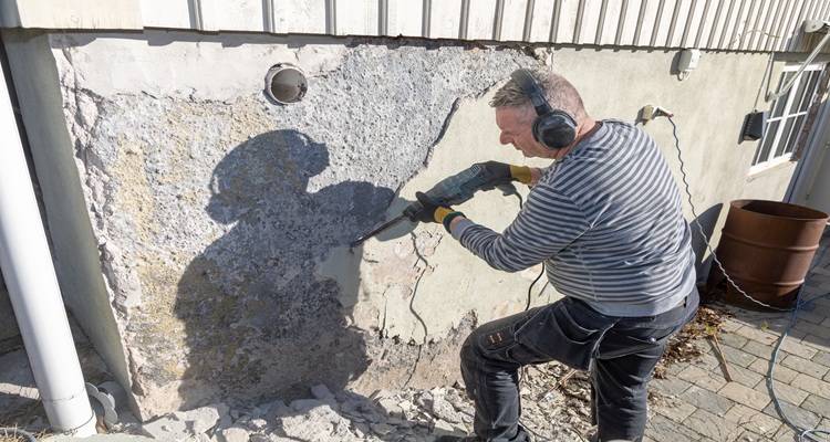 man using an SDS drill to remove render