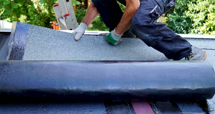 tradesperson is unrolling roofing felt on a job
