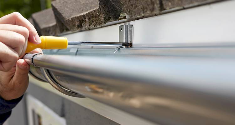closeup of a tradespeson is screwing in new metal guttering