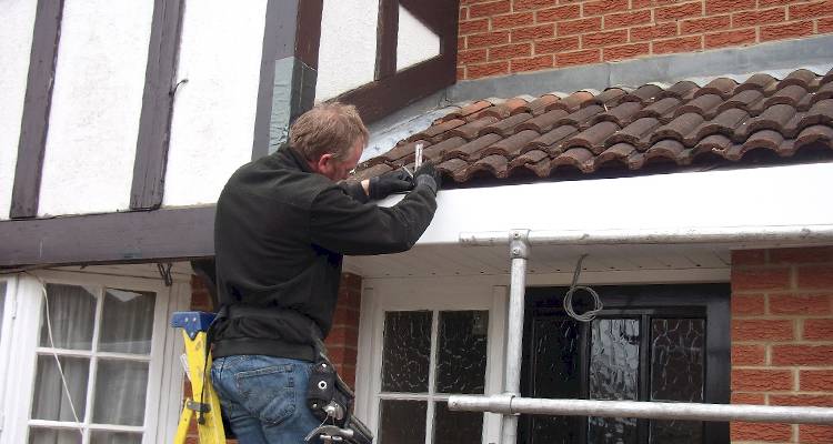 tradesperson standing on a ladder inspecting roofing