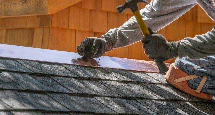 roofer preparing to hammer in a nail to secure a roof repair