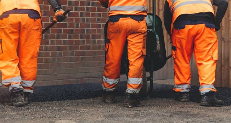 three men in orange laying tarmac