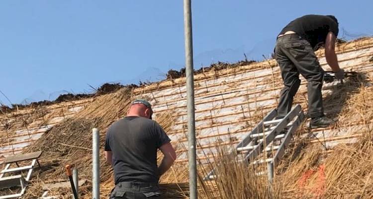 two tradespeople installing a thatched roof on a UK property